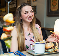 A young woman enjoys a burger and catch-up with friends at Poms